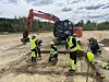 People in hi-vis gear working beside an excavator on a dirt site.