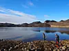 Two people walking by a lake with mountains in the distance