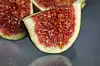 Close-up of sliced figs with red flesh and pale green skin on a dark background.