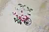 An embroidered floral motif in pink, red, and green on light-coloured fabric with a black stamp.