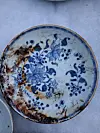 Blue and white floral ceramic plate with chips and stains on a plain surface.