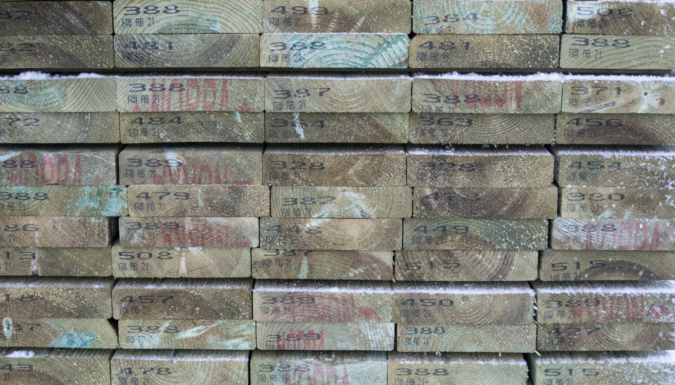 The ends of stacked decking boards showing markings and the green tint from treatment.