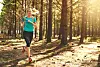 Woman running on a wooded trail in bright sunlight.