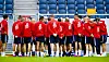 Football players in red tops stand in a huddle on a training pitch.