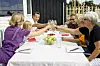 Adults and children toast with drinks around a table set with fruit at an outdoor meal.