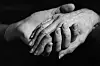 Black-and-white close-up of one hand holding an older person's hand.