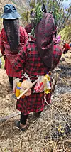 Two women in red patterned clothes carry bags of crackers, sweets and soft drinks on a dry hillside trail.