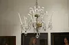 Crystal chandelier suspended in a gallery interior with framed portraits on the wall.