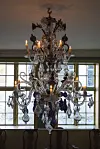 Decorative crystal chandelier hanging in front of tall windows.