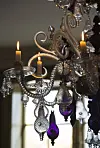 An ornate chandelier with lit candles and hanging crystal decorations in a dim room.
