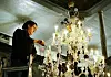 A man working on a large crystal chandelier in an ornate room.
