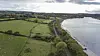 Aerial view of fields beside a river and a winding road under cloudy skies.
