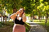 Ung kvinne med hodetelefoner står i en grønn park og lytter til musikk.