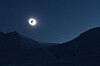 Mørk landskap med fjell og en lysende solring under total solformørkelse.