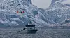 A rescue helicopter flies over a Norwegian Coast Guard ship on the sea near snow-covered mountains.