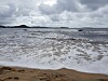 Sandstrand med lave bølger under en overskyet himmel.