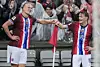 Erling Braut Haaland and Martin Ødegaard smile and hold each other's hands in the stadium during the match against Italy. It is raining. The audience can be seen in the background wearing raincoats.