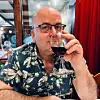 Portrait of Professor Arve Hjelseth with a flowered shirt and a glass of wine that he holds to his mouth.