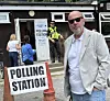 A polling station with a 'POLLING STATION' sign, two police officers, and several people outside a building.