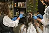 Two stylists apply hair dye to a client’s hair in a salon.