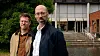 Two men standing outside a modern building with steps and glass windows.