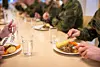 Soldiers sit at a mess hall table with plates of food and glasses of water at Ørland Main Air Station.