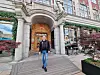 Person walking through an arched entrance of a historic building beside café tables and planters.