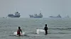 Two boys watch several ships on a hazy sea near the Strait of Hormuz.