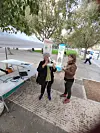 Two women stand by an outdoor information table, one wearing VR goggles during a deep renovation information session in Palma.