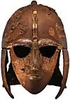 Ancient bronze helmet with a face mask and cheek guards on a white background.