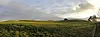 Wide green countryside under cloudy skies with a distant farmhouse and trees.