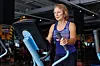 A woman over the age of 60 exercises on an elliptical machine in a modern gym.