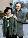 Smiling couple standing outdoors in winter clothing beside a building.