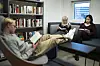 Students reading quietly in a school library beside bookshelves and a window.