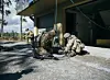 Camouflaged military medics kneel beside a casualty during an outdoor training exercise near a building.