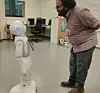 Suraj De bends toward Pepper, a humanoid robot, in a laboratory room.