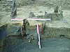 Excavation trench showing exposed layers of soil and clay with measuring rods laid across the site.