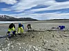Three archaeologists dig on a rocky shoreline near the sea.