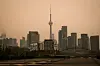 Toronto skyline with the CN Tower silhouetted against a smoky orange sky.
