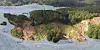 Aerial view of wooded land, earthworks, roads and a shoreline beside a body of water.