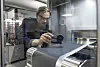 Researcher measuring a battery cathode layer with precision equipment in a laboratory.