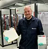 Researcher in a SINTEF lab holds two pouch cell batteries beside battery production machinery.