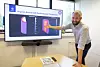 Researcher pointing at a screen showing a battery temperature simulation in a meeting room.