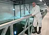 A person wearing a white protective suit stands on a walkway beside a large indoor fish tank.