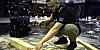 A crouching worker adjusts equipment on a wet workshop floor beside industrial machinery.