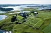 An aerial photograph of Avaldsnes Church and churchyard. The church is located on Karmøy, surrounded by green fields and the fjord.