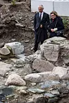 Two people in formal clothing walking over rocks and debris in an outdoor area.