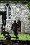 Dagfinn Skre standing and leaning on a shovel beside an excavator, wearing a hat.