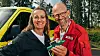 Two people stand outdoors beside a yellow emergency vehicle, holding an inhaler used for field pain relief.