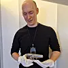 A man in a black shirt examines a handgun while wearing white gloves indoors.